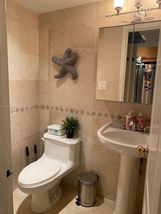 bathroom with toilet, a sink, backsplash, and tile walls