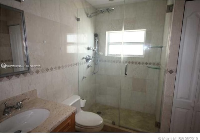 bathroom with toilet, a shower stall, tile walls, and vanity