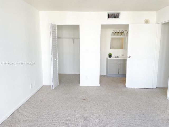 unfurnished bedroom featuring a walk in closet, a closet, light colored carpet, visible vents, and a textured ceiling