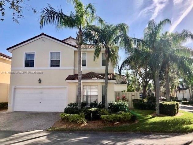mediterranean / spanish house featuring fence, stucco siding, an attached garage, a tile roof, and driveway