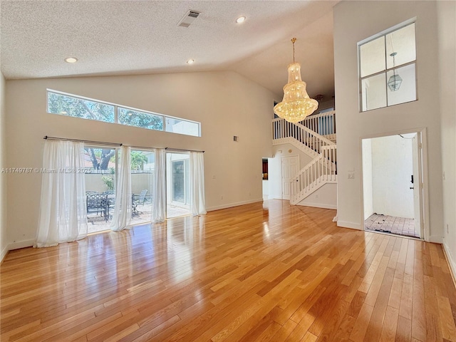 unfurnished living room with light wood finished floors, visible vents, a chandelier, stairway, and high vaulted ceiling