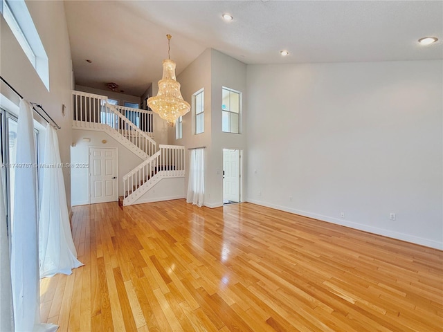 unfurnished living room with high vaulted ceiling, a chandelier, stairs, and light wood-style floors