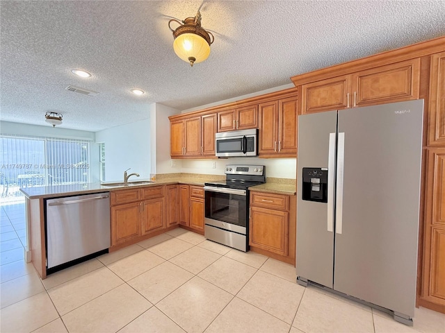 kitchen featuring stainless steel appliances, visible vents, a sink, brown cabinetry, and a textured ceiling