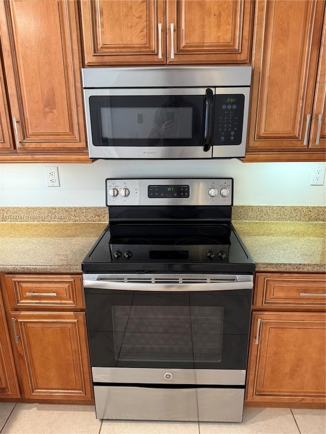 kitchen with brown cabinets, light stone countertops, appliances with stainless steel finishes, and light tile patterned floors