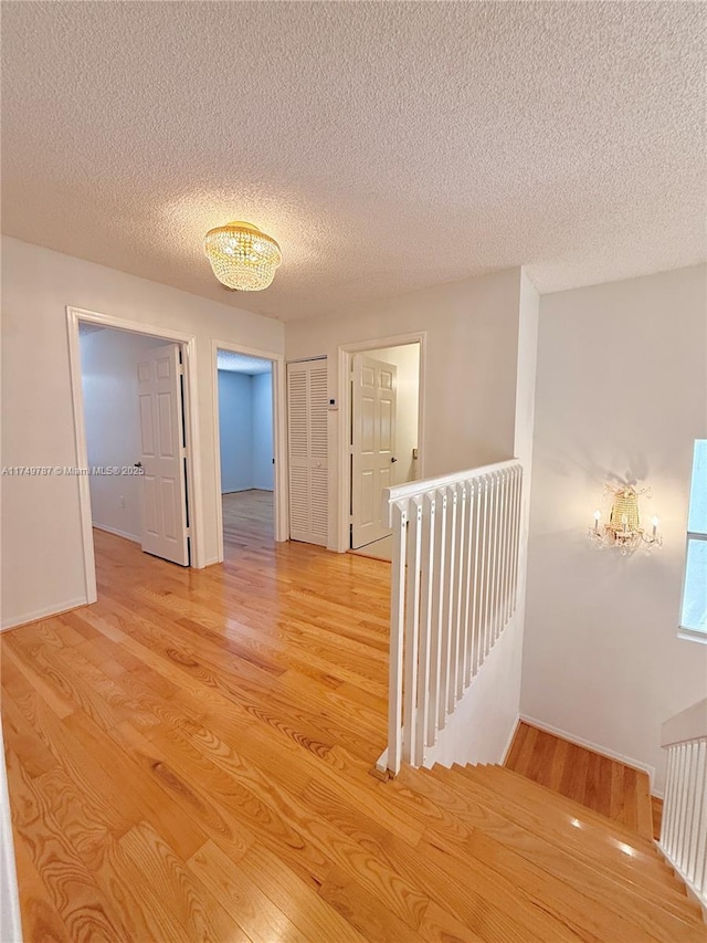 hall featuring wood finished floors, a textured ceiling, baseboards, and an upstairs landing