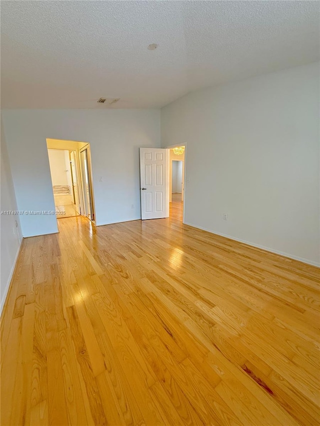 empty room with light wood-style floors, a textured ceiling, and baseboards