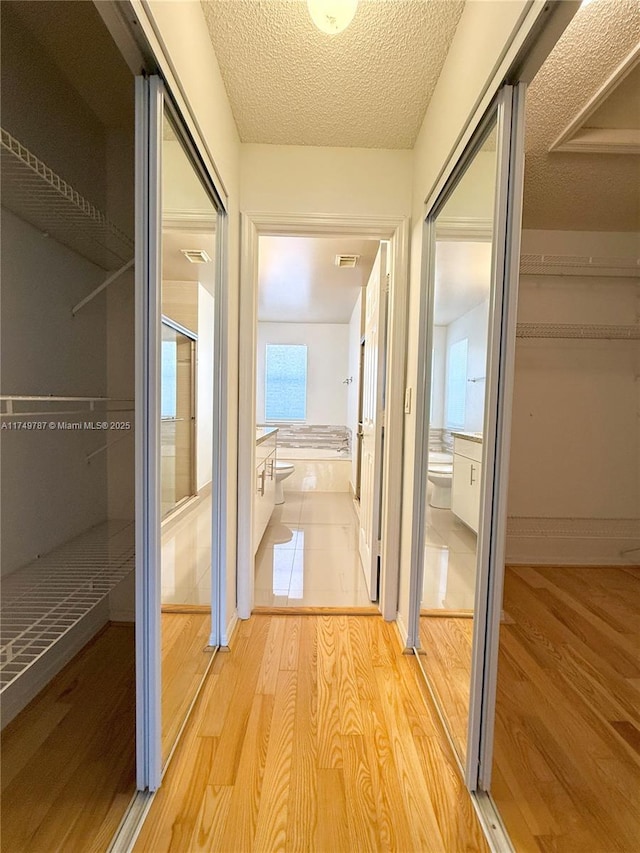 hall featuring wood finished floors, visible vents, and a textured ceiling