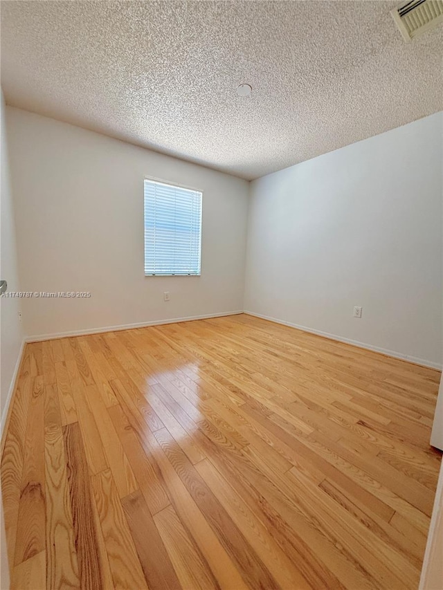 unfurnished room featuring light wood-type flooring, baseboards, visible vents, and a textured ceiling