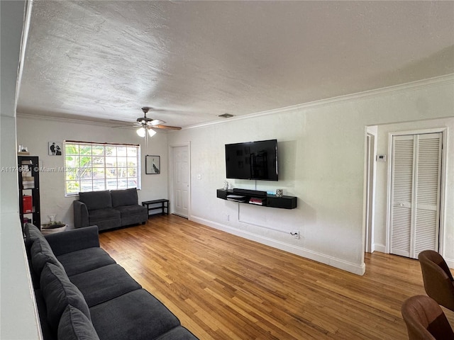 living room featuring baseboards, a ceiling fan, ornamental molding, wood finished floors, and a textured ceiling