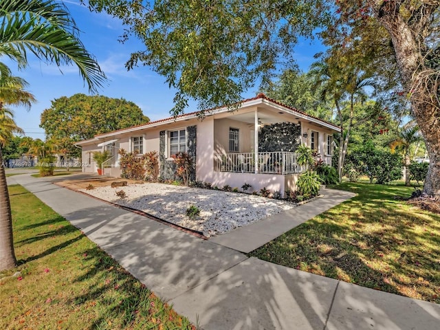 view of front of house with a porch, a front yard, a tile roof, and stucco siding