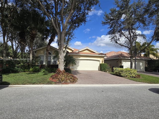 view of front of home with decorative driveway, stucco siding, an attached garage, a tiled roof, and a front lawn