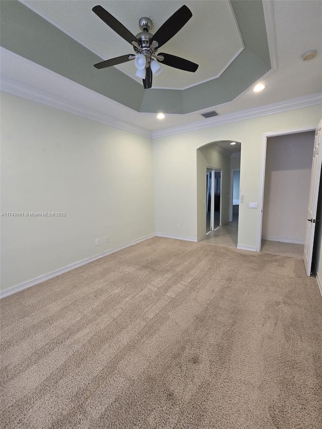 unfurnished room with a tray ceiling, arched walkways, crown molding, and light colored carpet