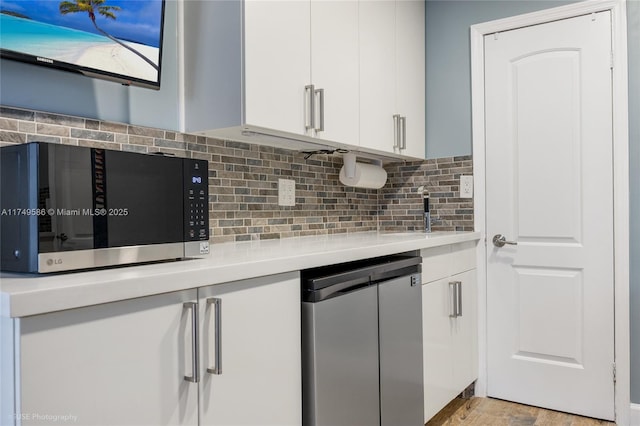 kitchen with stainless steel microwave, backsplash, white cabinetry, and light countertops