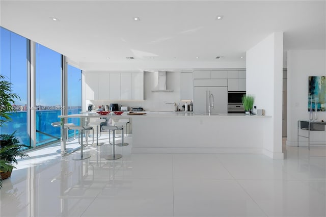 kitchen featuring paneled refrigerator, white cabinets, light countertops, wall chimney range hood, and modern cabinets