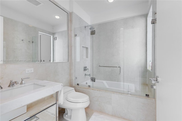 bathroom with visible vents, toilet, tiled shower / bath combo, vanity, and tile walls