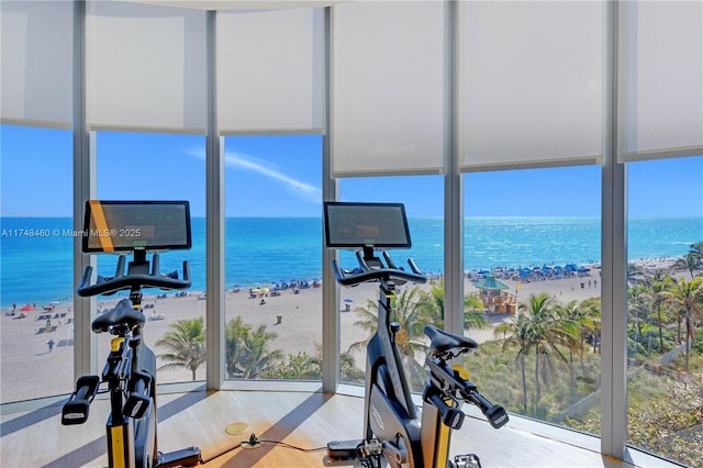 exercise room with a water view, expansive windows, a beach view, and wood finished floors