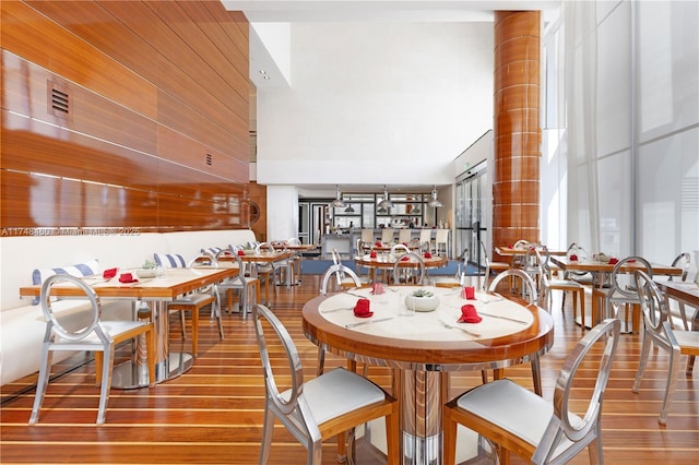 dining space with wooden walls, a high ceiling, and wood finished floors