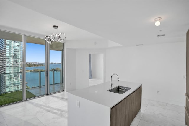 kitchen with floor to ceiling windows, light countertops, a water view, a kitchen island with sink, and a sink