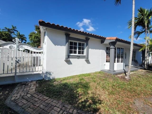 view of property exterior with a tile roof, a yard, central AC, and stucco siding