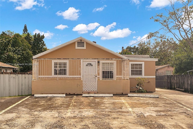 bungalow featuring uncovered parking, stucco siding, and fence