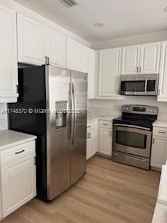 kitchen with light wood finished floors, light countertops, appliances with stainless steel finishes, and white cabinetry