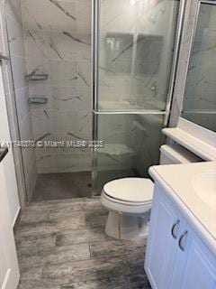 bathroom featuring toilet, a marble finish shower, and vanity