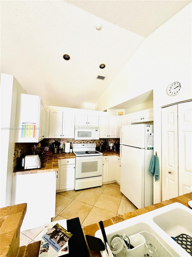 kitchen with tile counters, lofted ceiling, tasteful backsplash, white cabinets, and white appliances