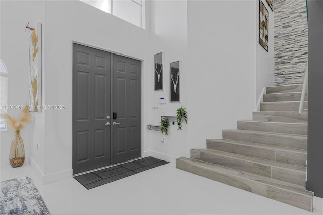 tiled foyer entrance with stairs, a high ceiling, and baseboards