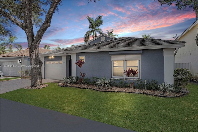 single story home with a garage, a yard, driveway, and stucco siding