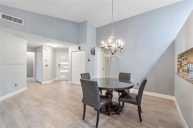 dining area featuring light wood-style floors, visible vents, a textured ceiling, and baseboards