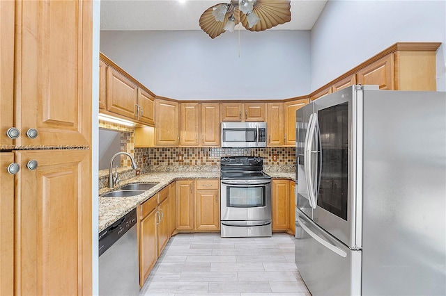 kitchen with light stone countertops, backsplash, stainless steel appliances, and a sink