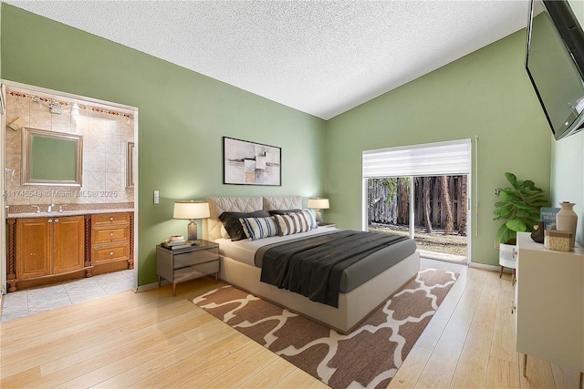 bedroom with light wood-style flooring, a sink, vaulted ceiling, a textured ceiling, and access to outside