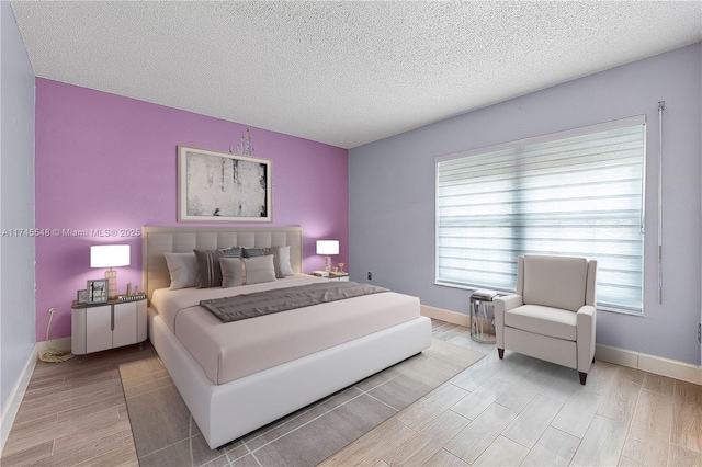 bedroom with light wood-style floors, baseboards, and a textured ceiling