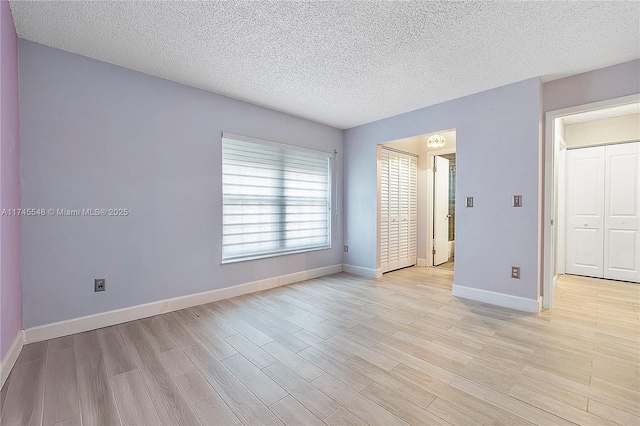 unfurnished bedroom featuring a textured ceiling, light wood-type flooring, and baseboards