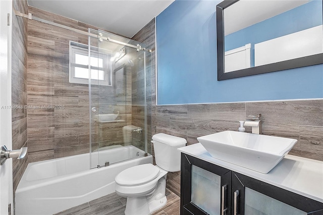 bathroom featuring toilet, wood finished floors, vanity, tile walls, and combined bath / shower with glass door