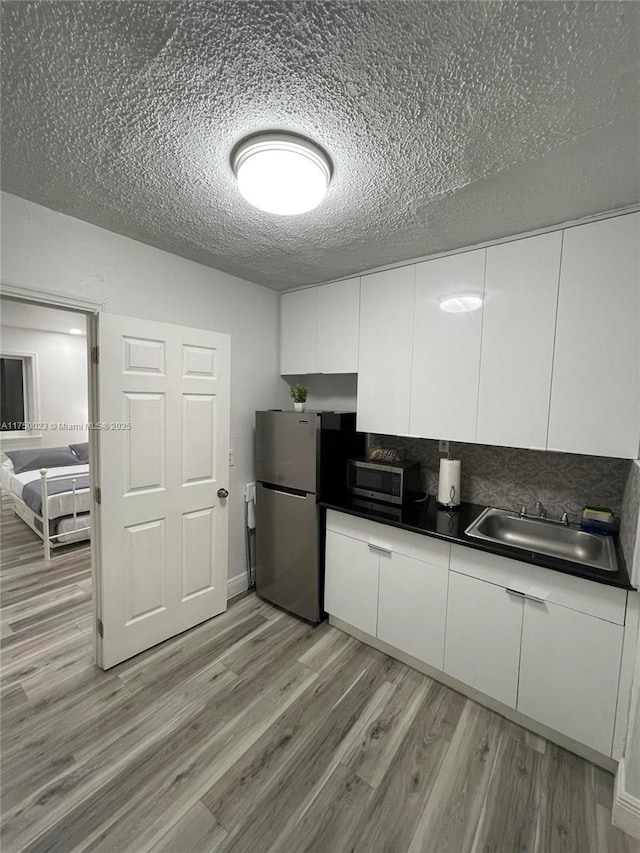 kitchen with stainless steel appliances, a sink, white cabinets, light wood-type flooring, and dark countertops