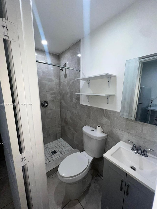 bathroom with toilet, a shower stall, tile walls, and vanity