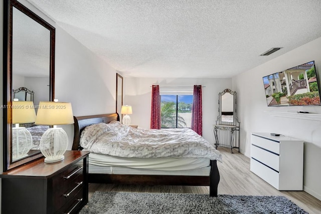 bedroom featuring visible vents, light wood-style flooring, and a textured ceiling