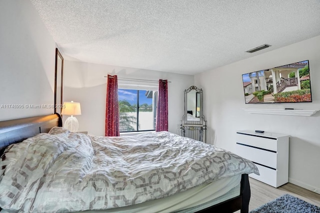 bedroom with light wood finished floors, visible vents, and a textured ceiling