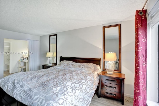 bedroom with light wood-type flooring, ensuite bath, baseboards, and a textured ceiling