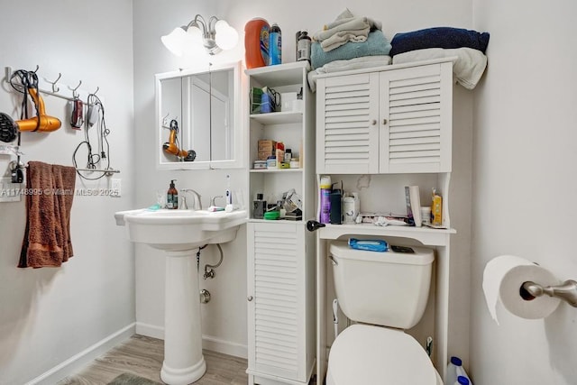 half bathroom with baseboards, toilet, and wood finished floors