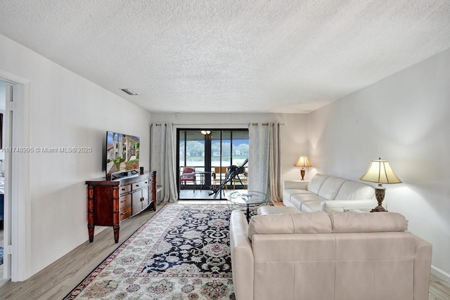 living area with a textured ceiling, wood finished floors, visible vents, and baseboards