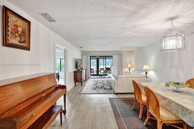 dining space with a textured ceiling, wood finished floors, visible vents, and a notable chandelier