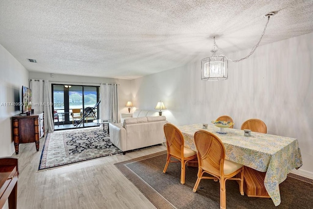 dining area with a textured ceiling, wood finished floors, visible vents, and a notable chandelier