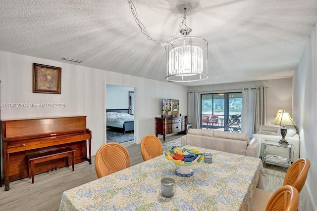 dining room with a chandelier, light wood-style flooring, a textured ceiling, and visible vents