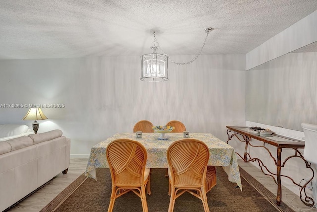 dining area with an inviting chandelier, a textured ceiling, and wood finished floors