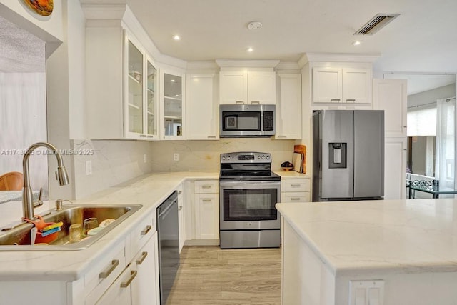 kitchen featuring appliances with stainless steel finishes, visible vents, glass insert cabinets, and light stone counters