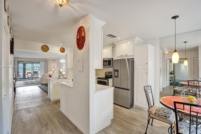 kitchen with appliances with stainless steel finishes, open floor plan, a peninsula, light countertops, and white cabinetry