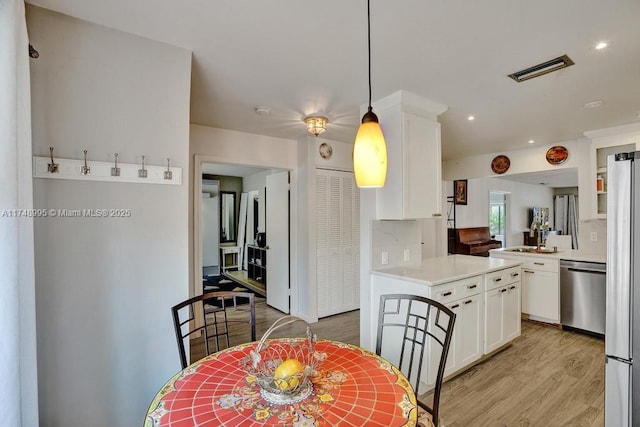 kitchen with light wood finished floors, light countertops, hanging light fixtures, appliances with stainless steel finishes, and white cabinetry