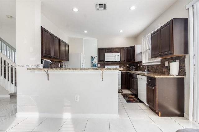 kitchen featuring visible vents, a sink, white appliances, a peninsula, and a kitchen breakfast bar